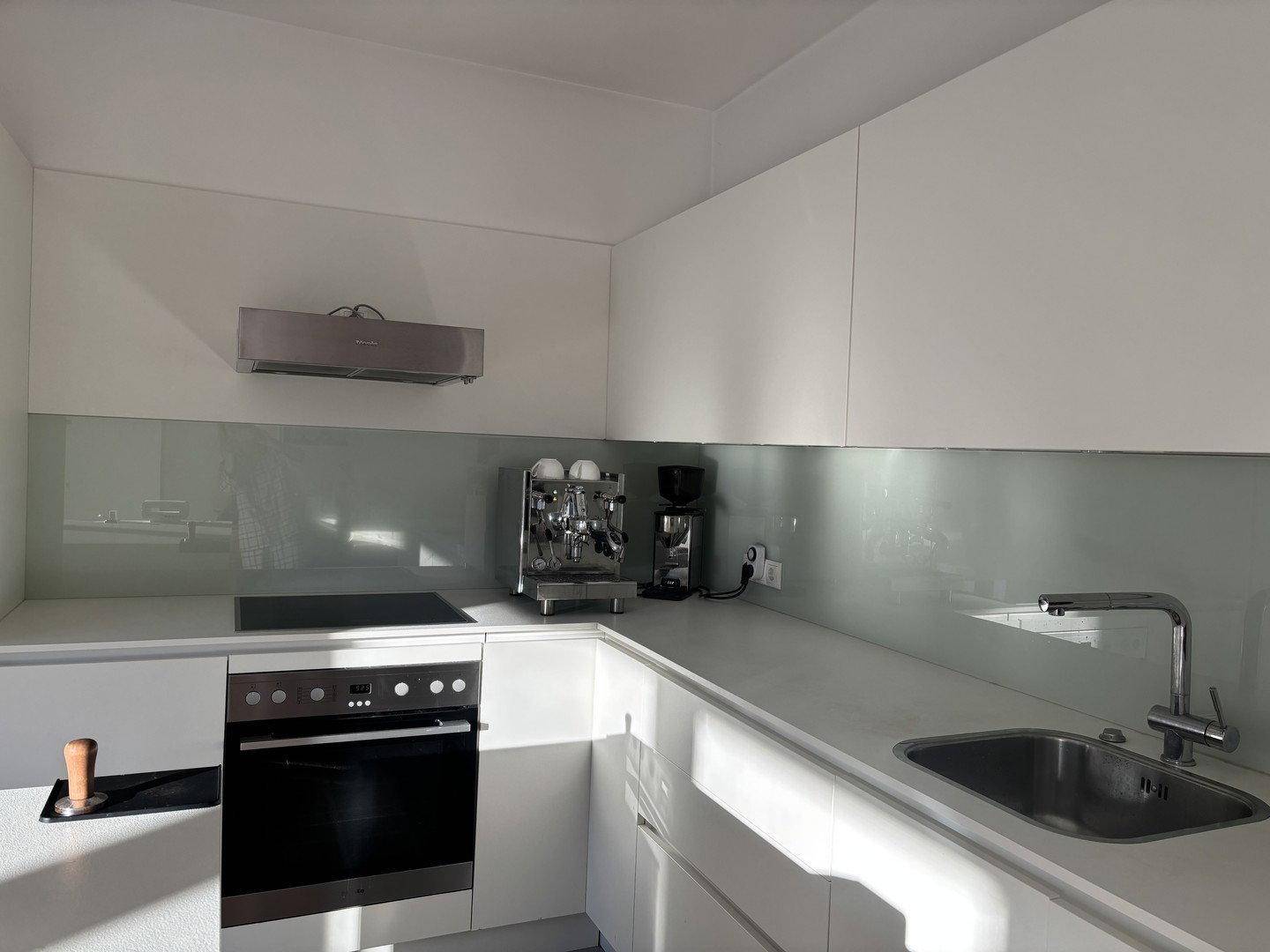 Helle, moderne Küche mit weißer Arbeitsplatte, Induktionskochfeld und Spülbecken.