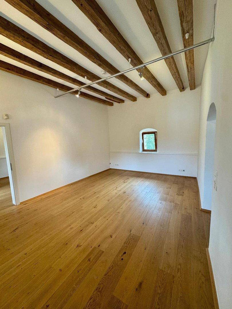 Geräumiger Raum mit sichtbaren Holzbalken an der Decke und hellem Holzboden.