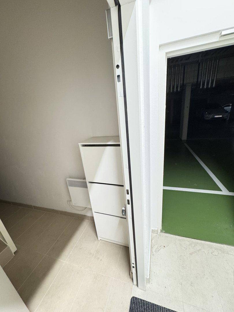 Eingangsbereich mit weißem Schrank und Heizung, der zur Tiefgarage führt.