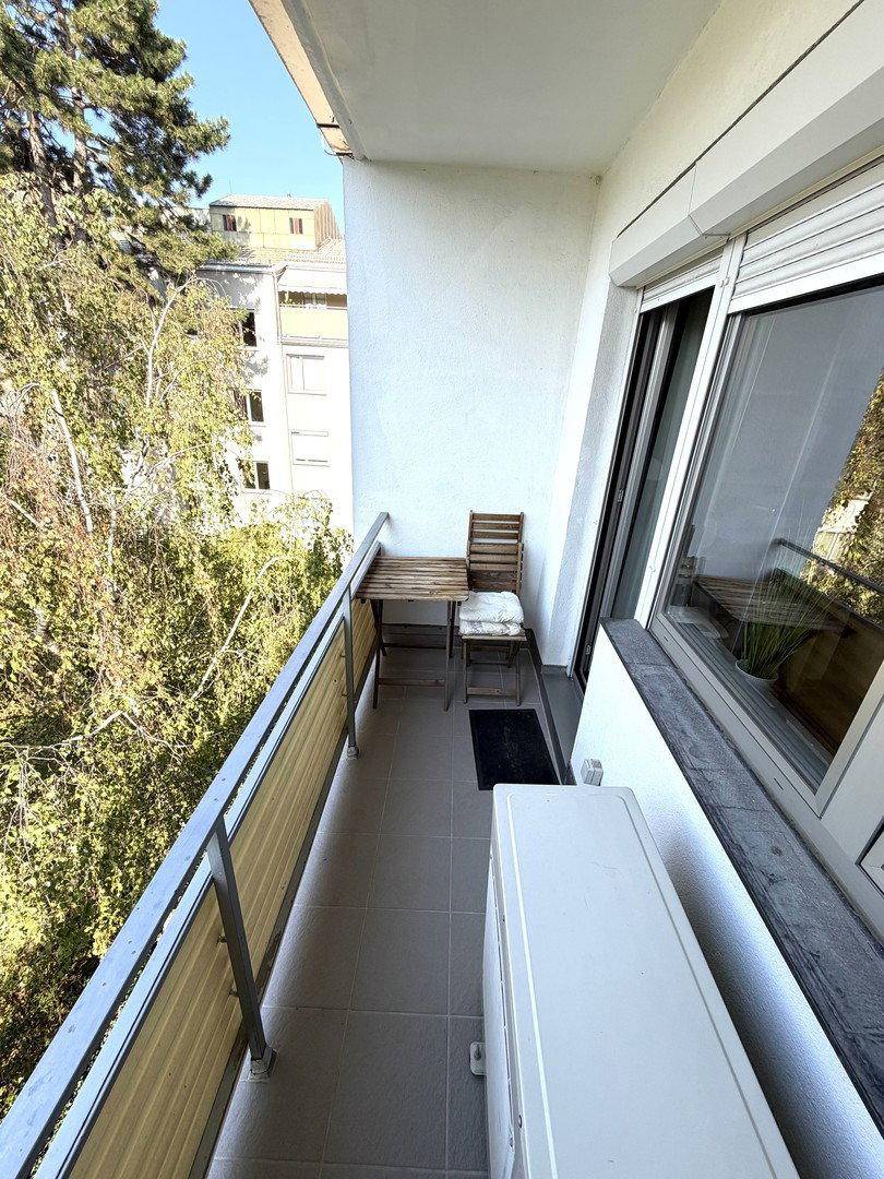 Kleiner Balkon mit Sitzgelegenheiten und Blick auf die umliegenden Gebäude und Bäume.