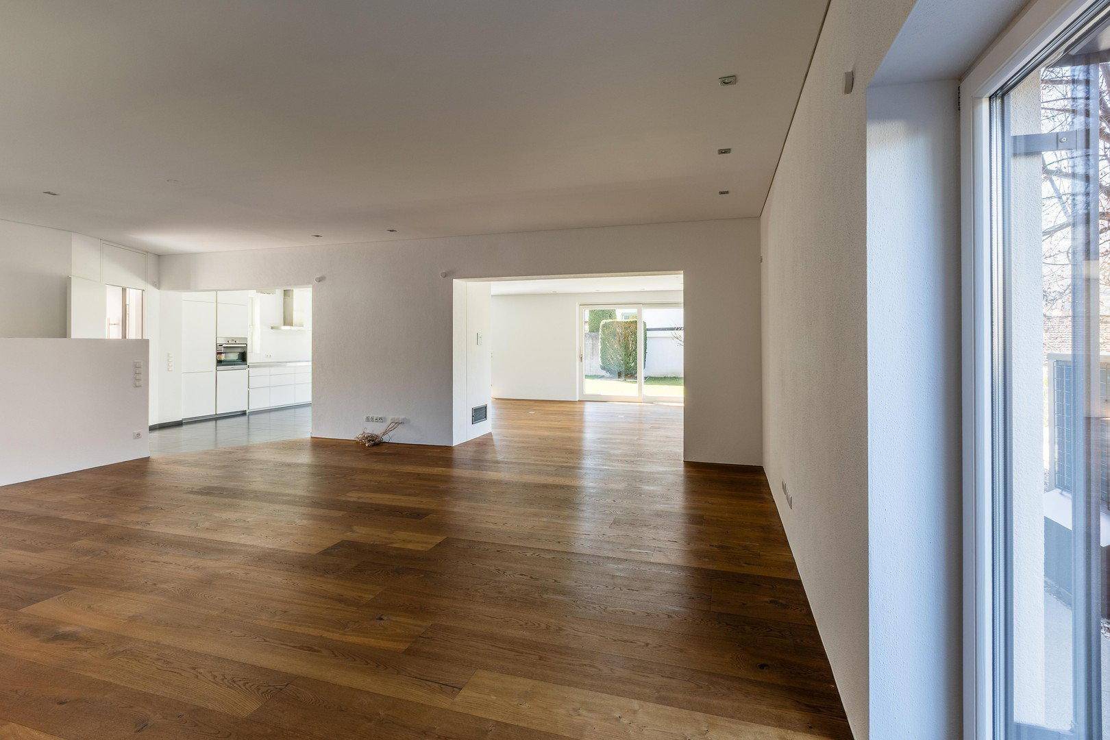 Geräumiger, heller Wohnbereich mit Holzboden und großen Fenstern, bereit zur individuellen Gestaltung.