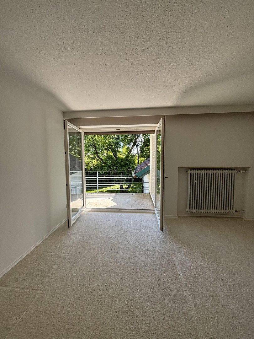 Helles Zimmer mit Teppichboden und großen Flügeltüren zum Balkon.