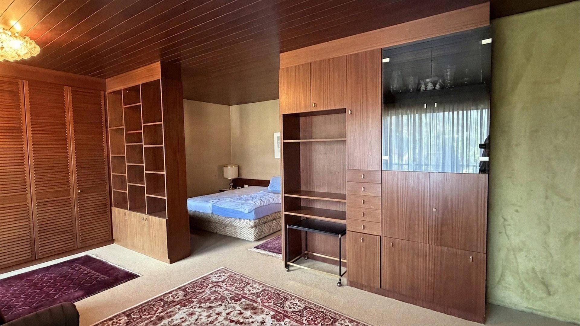 Schlafzimmer mit Holzeinbaumöbeln, Teppichboden und Blick auf das Bett im Hintergrund.
