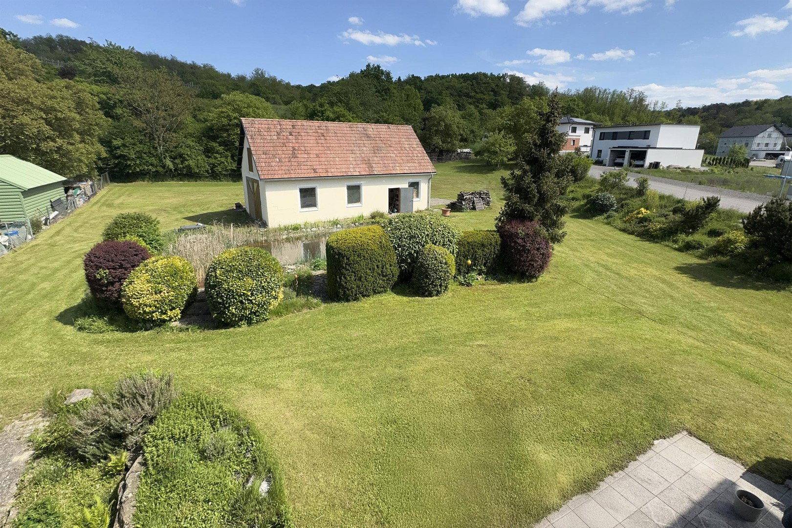 Großer, gepflegter Gartenbereich mit Rasenfläche und einem Nebengebäude im Hintergrund.