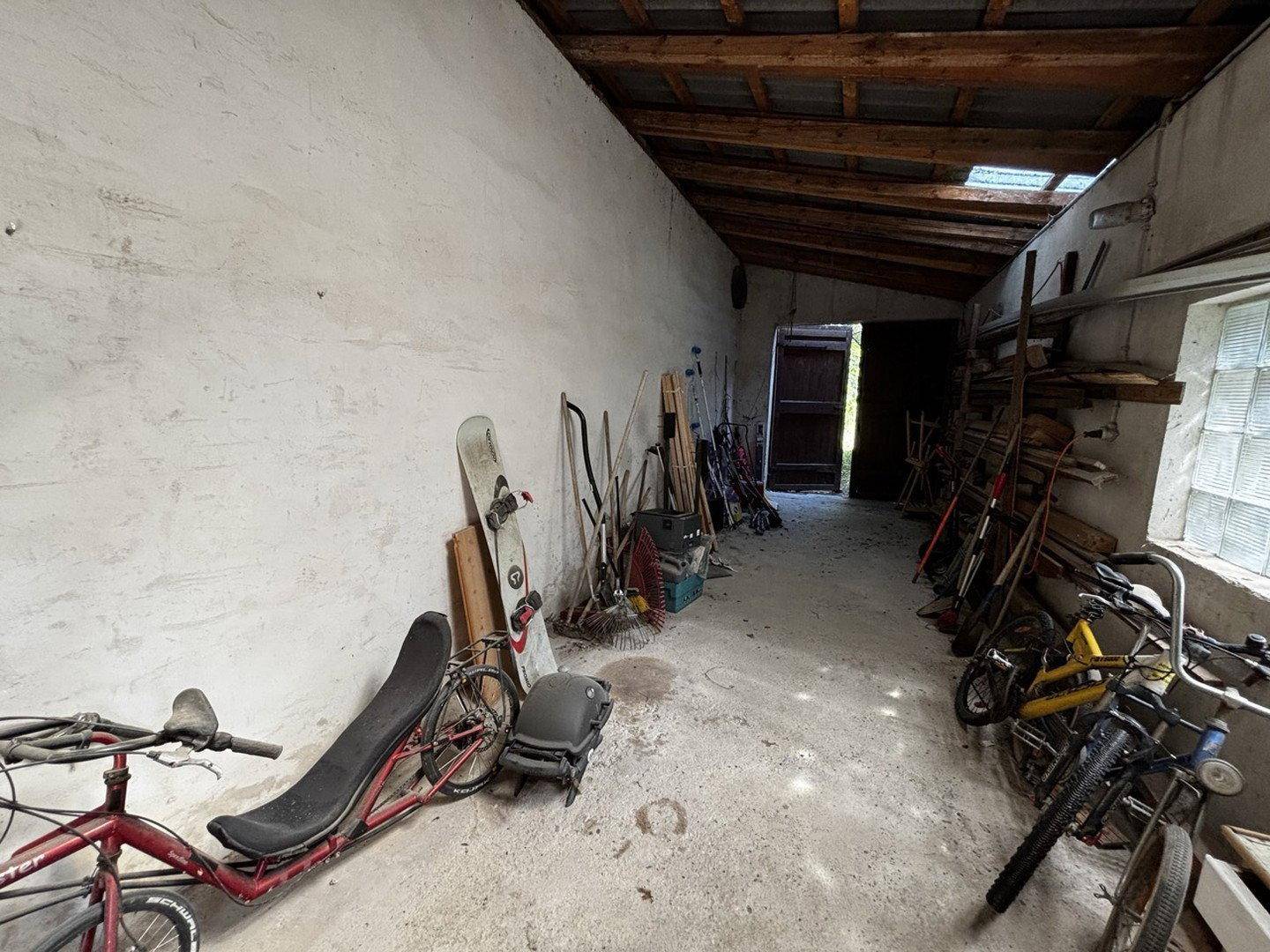 Langer Lagerraum mit Fahrrädern, Sportgeräten und einem Holzdach.