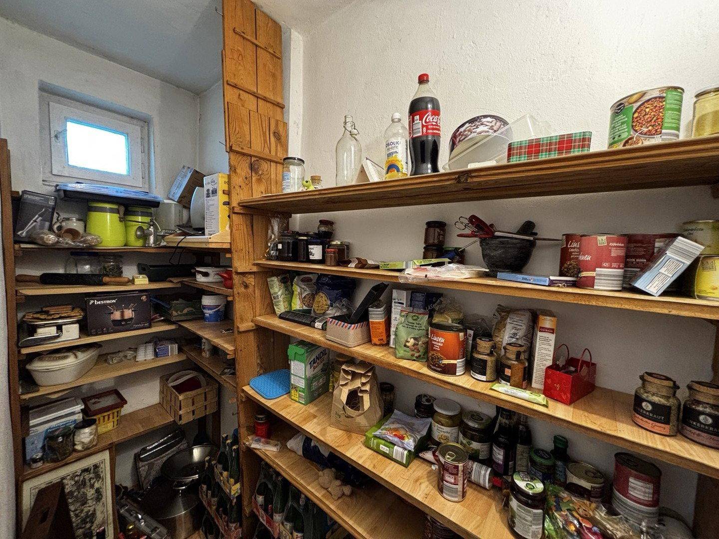 Gut organisierte Speisekammer mit vielen Regalen für Vorräte und einem kleinen Fenster.