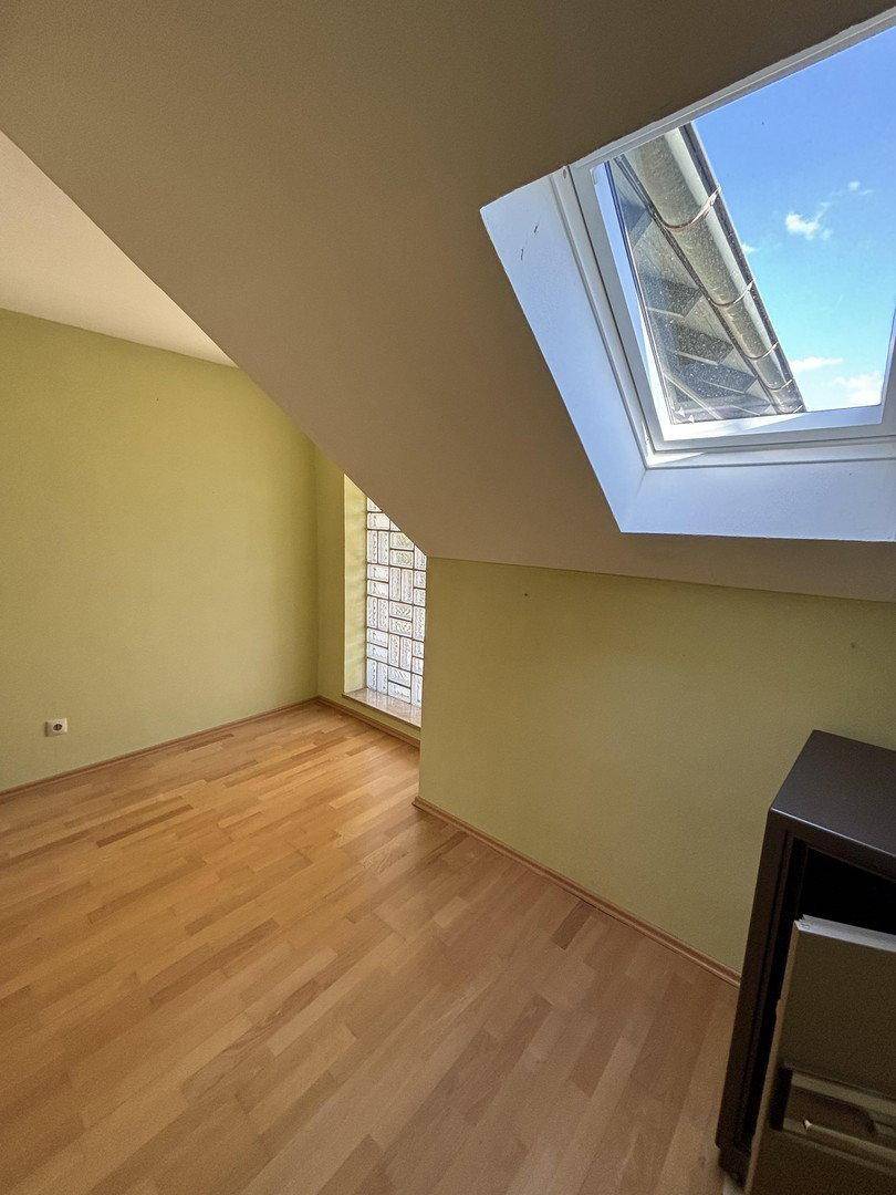 Dachzimmer mit Holzboden, Dachfenster und schrägen Wänden.
