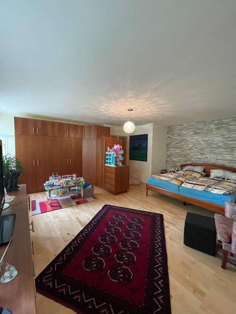 Geräumiges Schlafzimmer mit Holzboden, großer Schrankwand und dekorativer Steinwand hinter dem Bett.