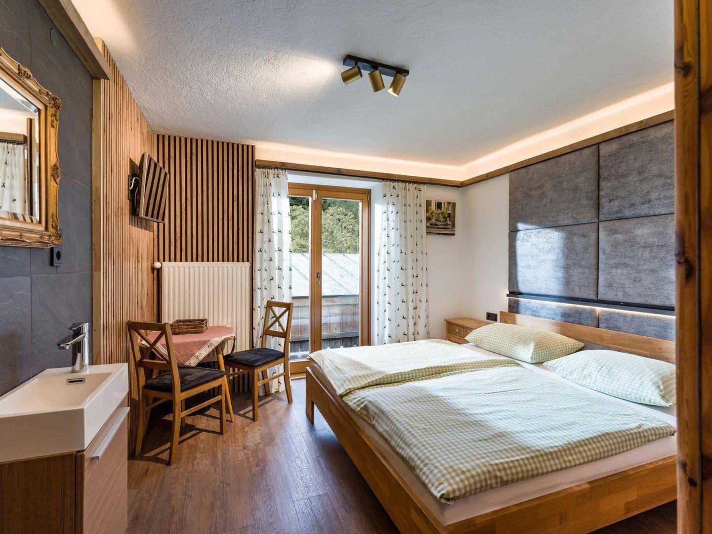 Schlafzimmer im alpinen Stil mit Doppelbett, Holzboden und kleinem Waschbecken.
