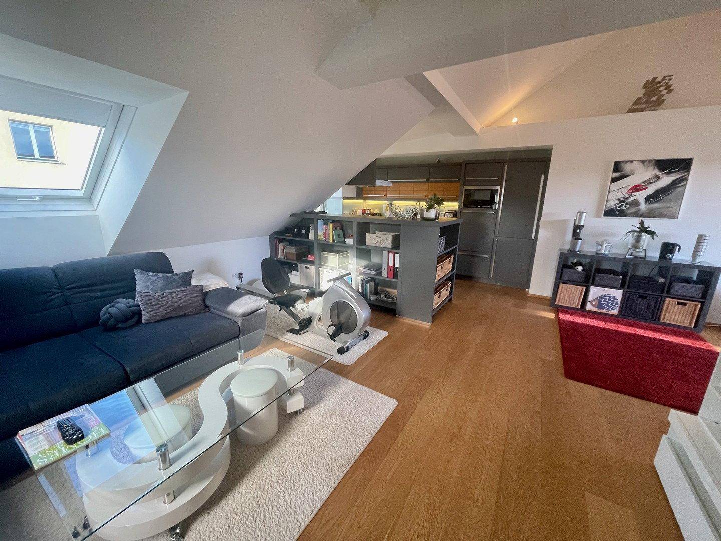 Offener Wohnbereich mit Sofa, Couchtisch und Heimtrainer, angrenzend an die Küche.