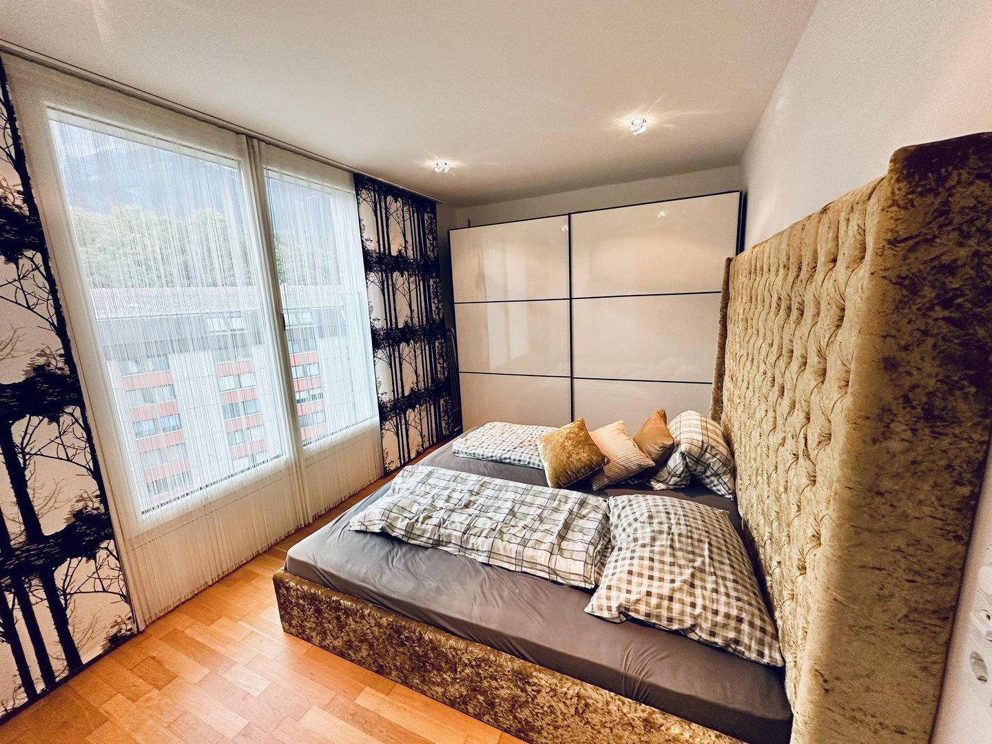 Schlafzimmer mit großem Bett, Holzboden und Einbauschränken, hell durch große Fenster.