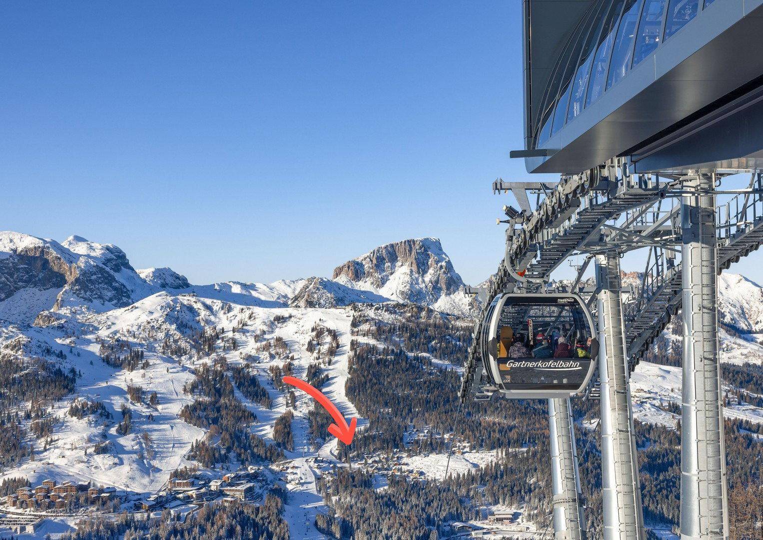 Luftaufnahme einer schneebedeckten Berglandschaft mit Skiliften, Pisten und einem Dorf.