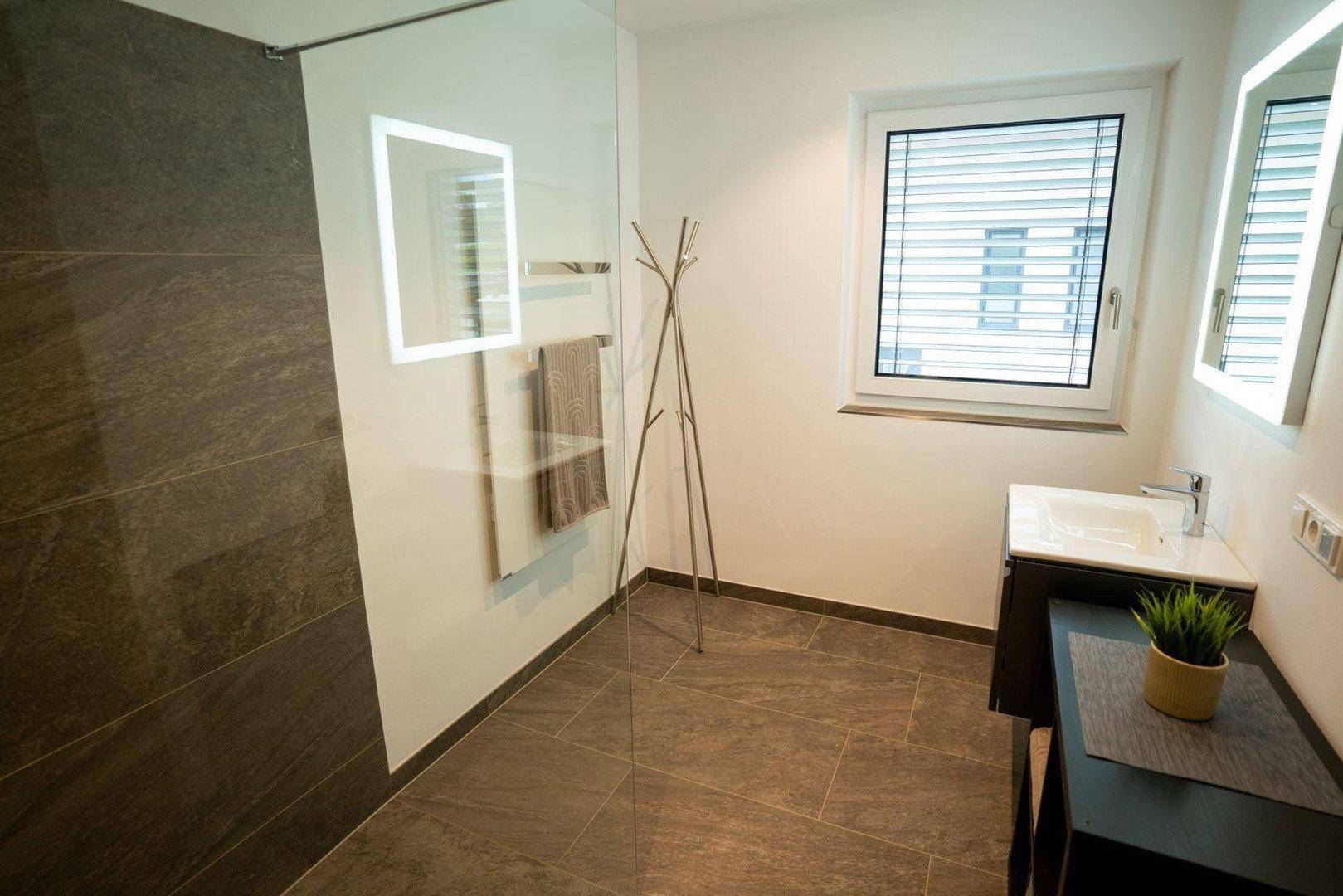 Helles Badezimmer mit großer begehbarer Dusche, Fenster und modernem Waschbecken.