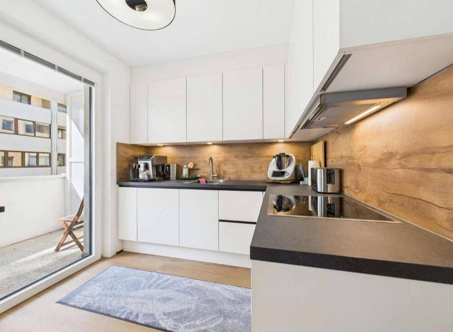 Moderne Küche mit weißen Schränken, Holzakzenten und Zugang zum Balkon.