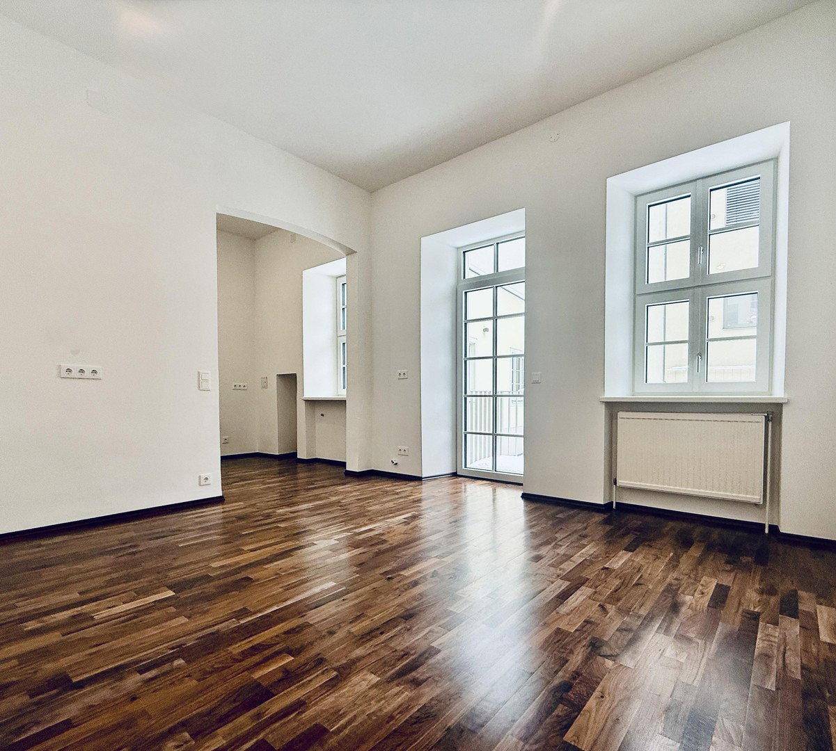 Lichtdurchflutetes Wohnzimmer mit Parkettboden und Zugang zu einem französischen Balkon.
