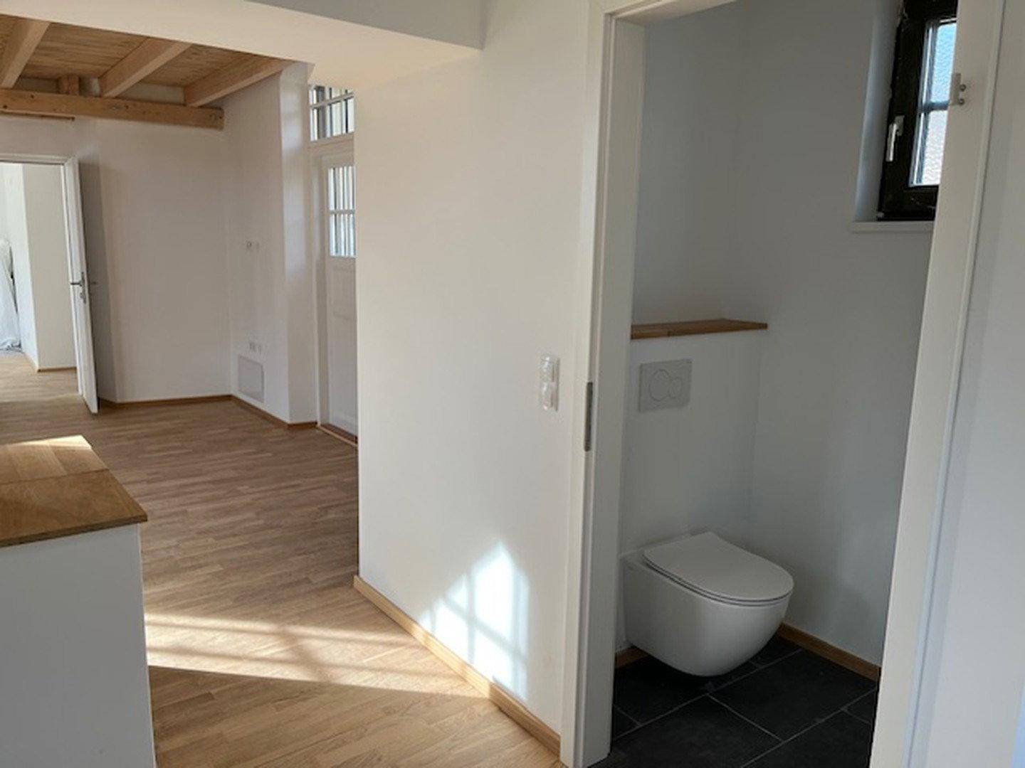 Modernes Gäste-WC mit Wand-WC, kleinem Fenster und dunklem Fliesenboden.