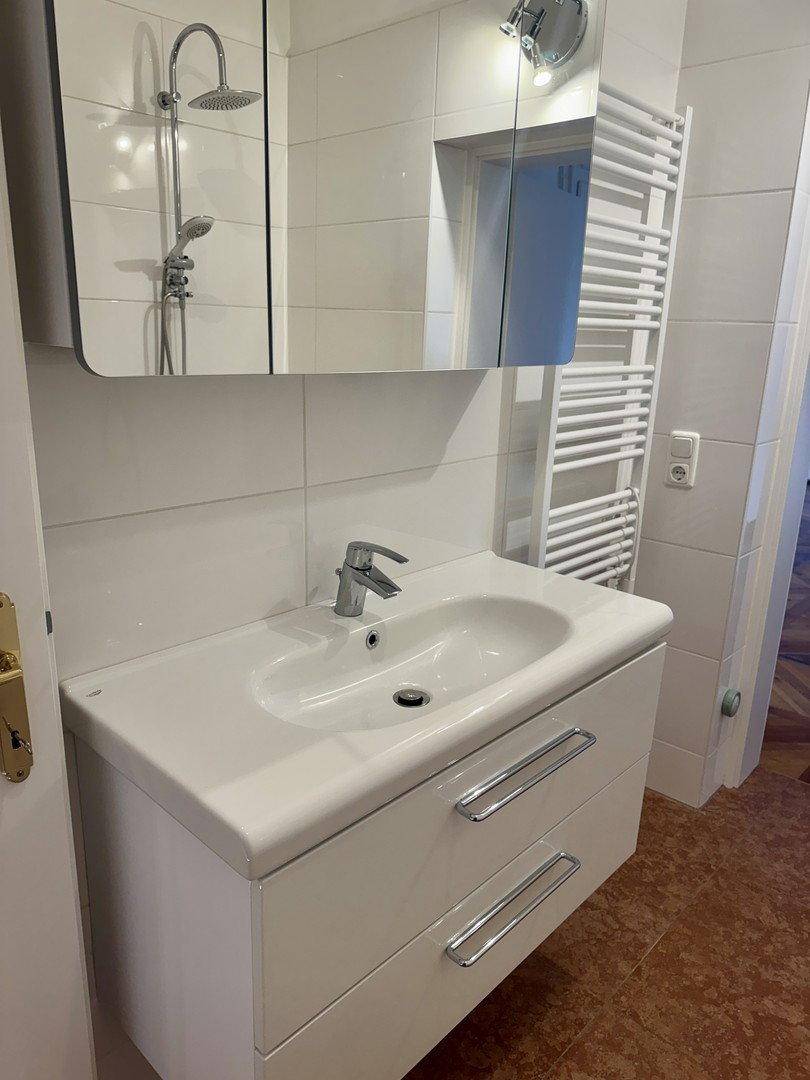 Waschtisch mit Unterschrank, Spiegelschrank und beheiztem Handtuchhalter im Badezimmer.