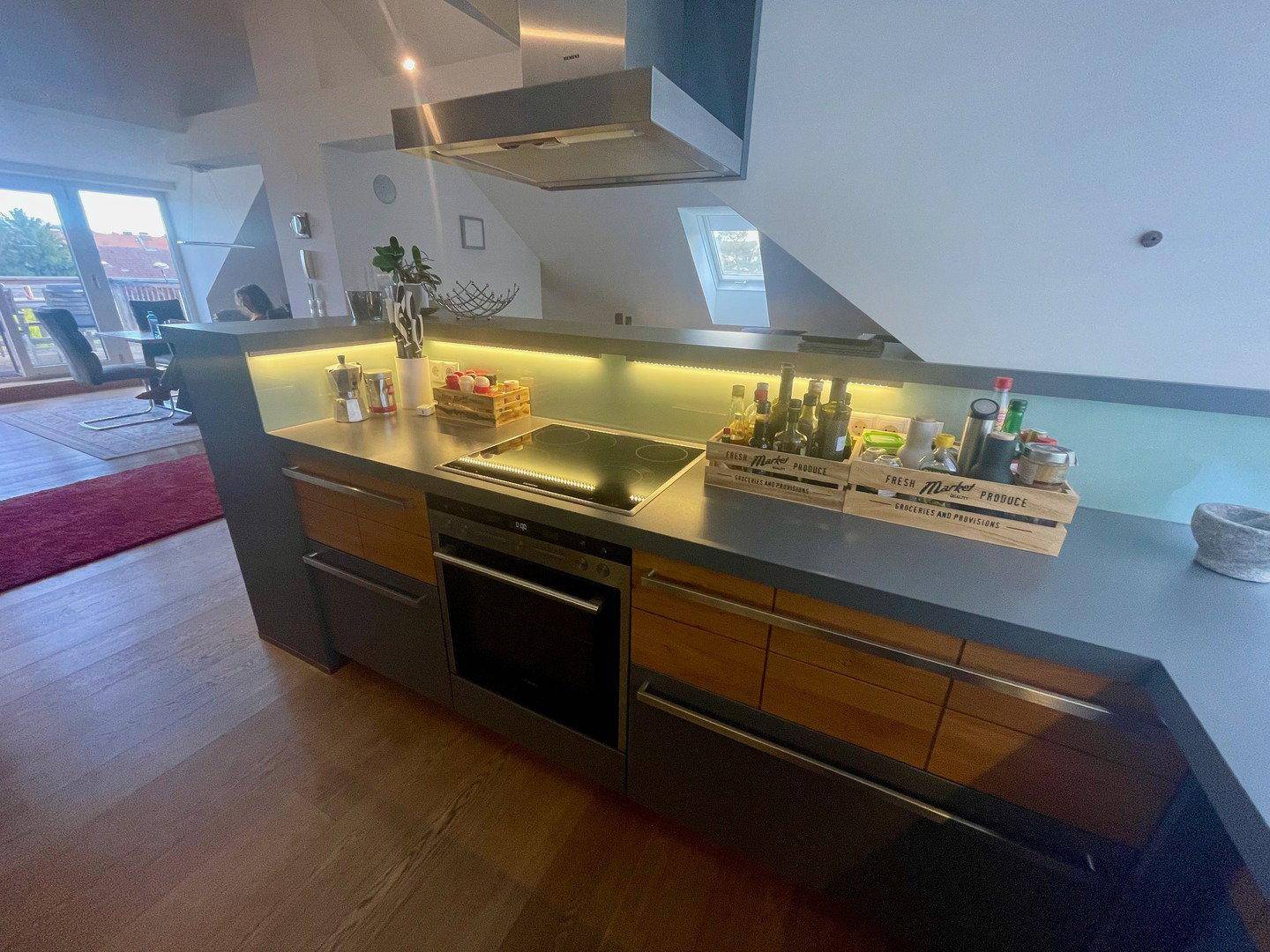 Küchenzeile mit integriertem Kochfeld und Backofen, beleuchteter Rückwand und Holzboden.