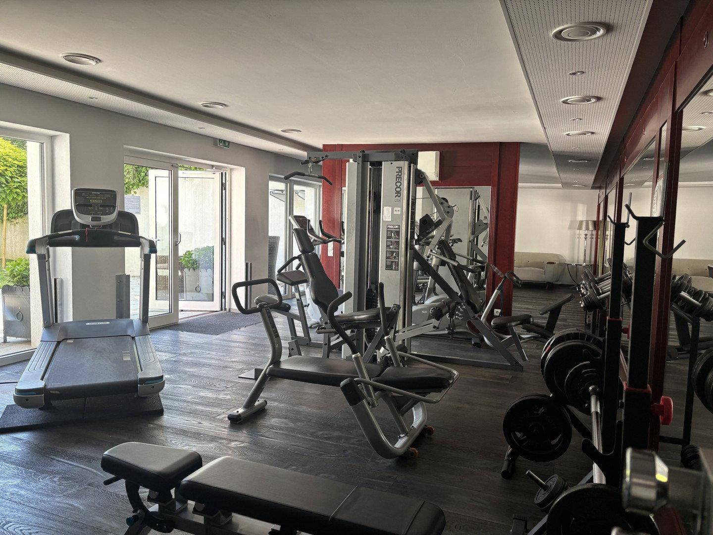 Gut ausgestatteter Fitnessraum mit verschiedenen Trainingsgeräten und großen Fenstern.