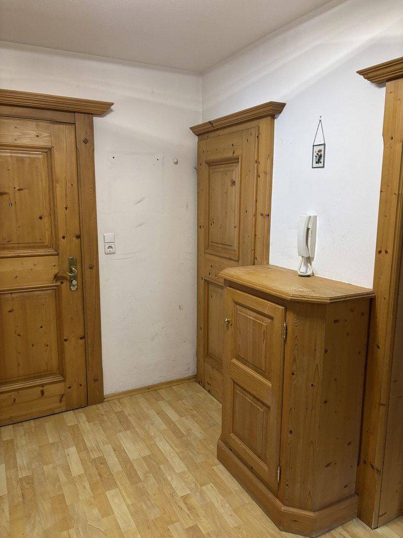 Flur mit traditionellen Holztüren und einem kleinen Holzschrank auf hellem Laminatboden.