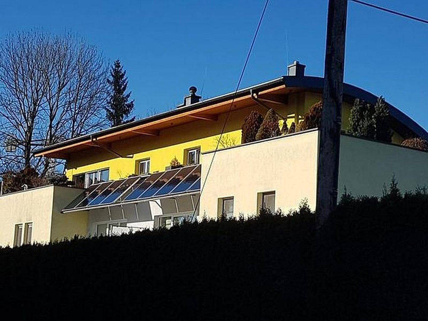 Modernes Wohnhaus mit gelber Fassade, Holzelementen und Solarpaneelen auf dem Dach.