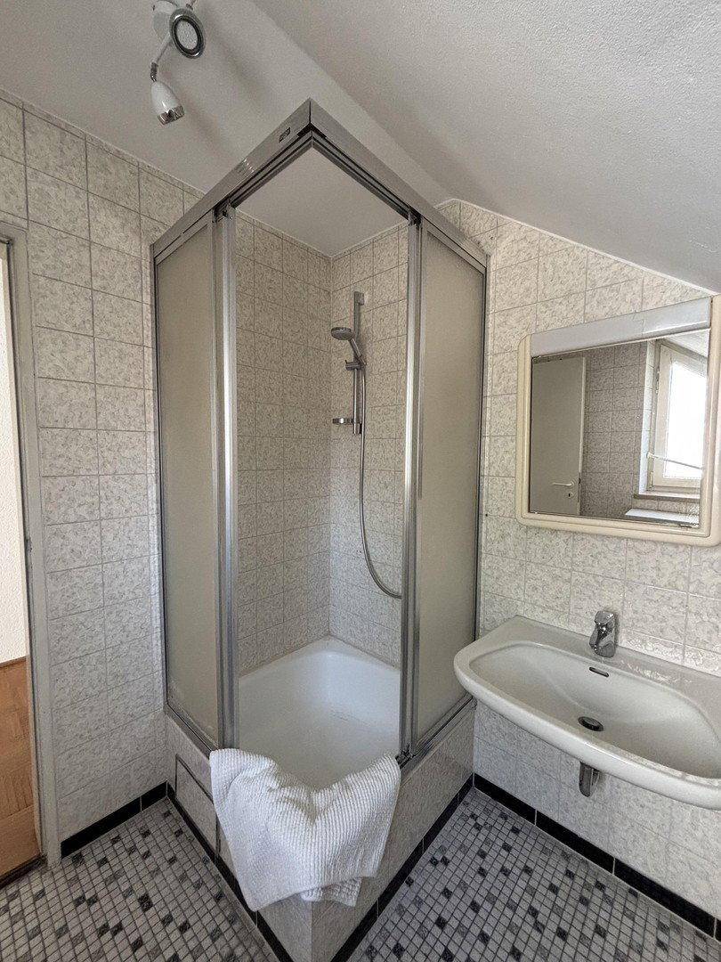 Badezimmer mit Duschkabine, Waschbecken und Fliesen im Retro-Stil.
