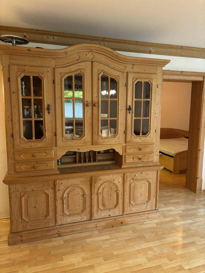 Großer traditioneller Holzschrank mit Glasvitrinen und Blick in ein angrenzendes Schlafzimmer.