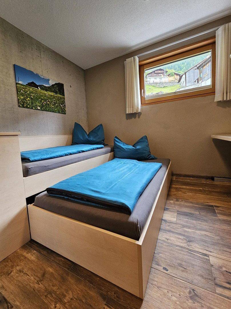 Gemütliches Schlafzimmer mit zwei Einzelbetten, Holzboden und Blick auf die grüne Landschaft.