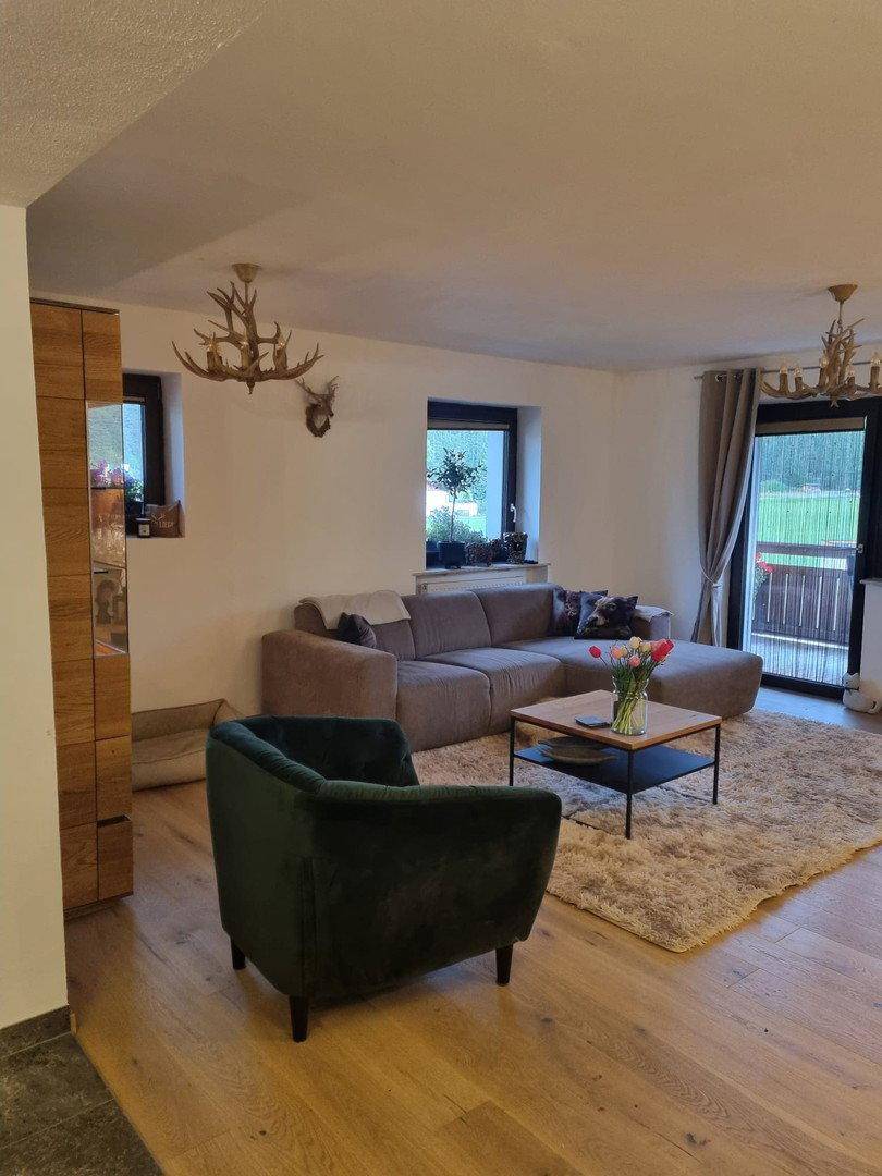 Geräumiges Wohnzimmer mit Ecksofa, grünem Sessel und Balkonzugang, Holzboden.