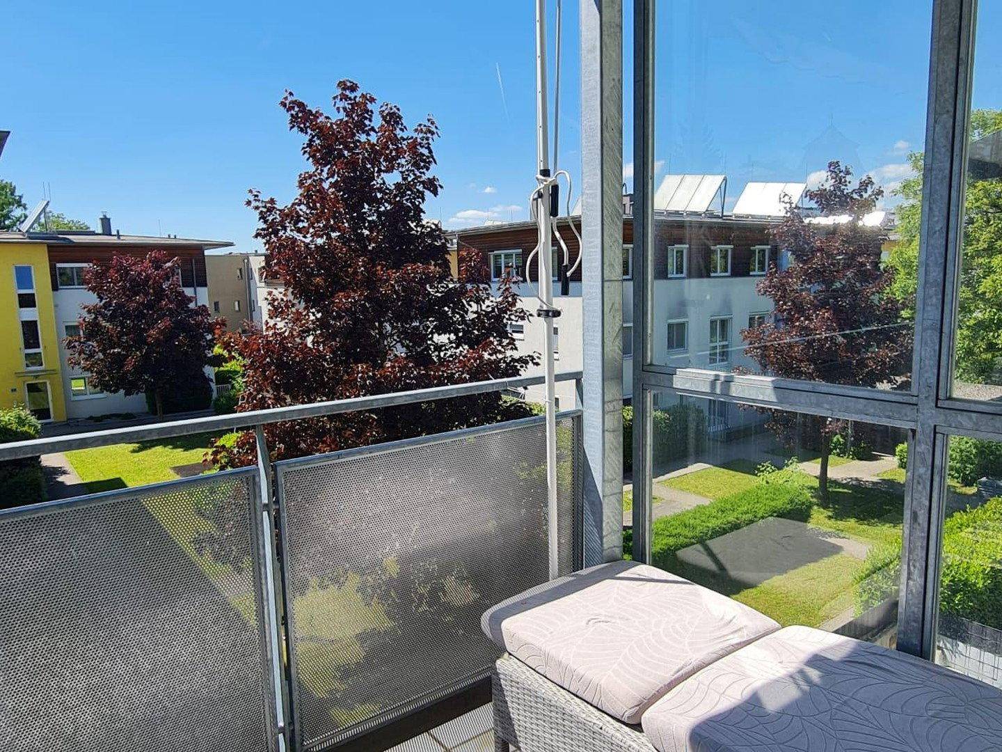 Heller Balkon mit Glasbrüstung und weitem Blick über die Wohnanlage.