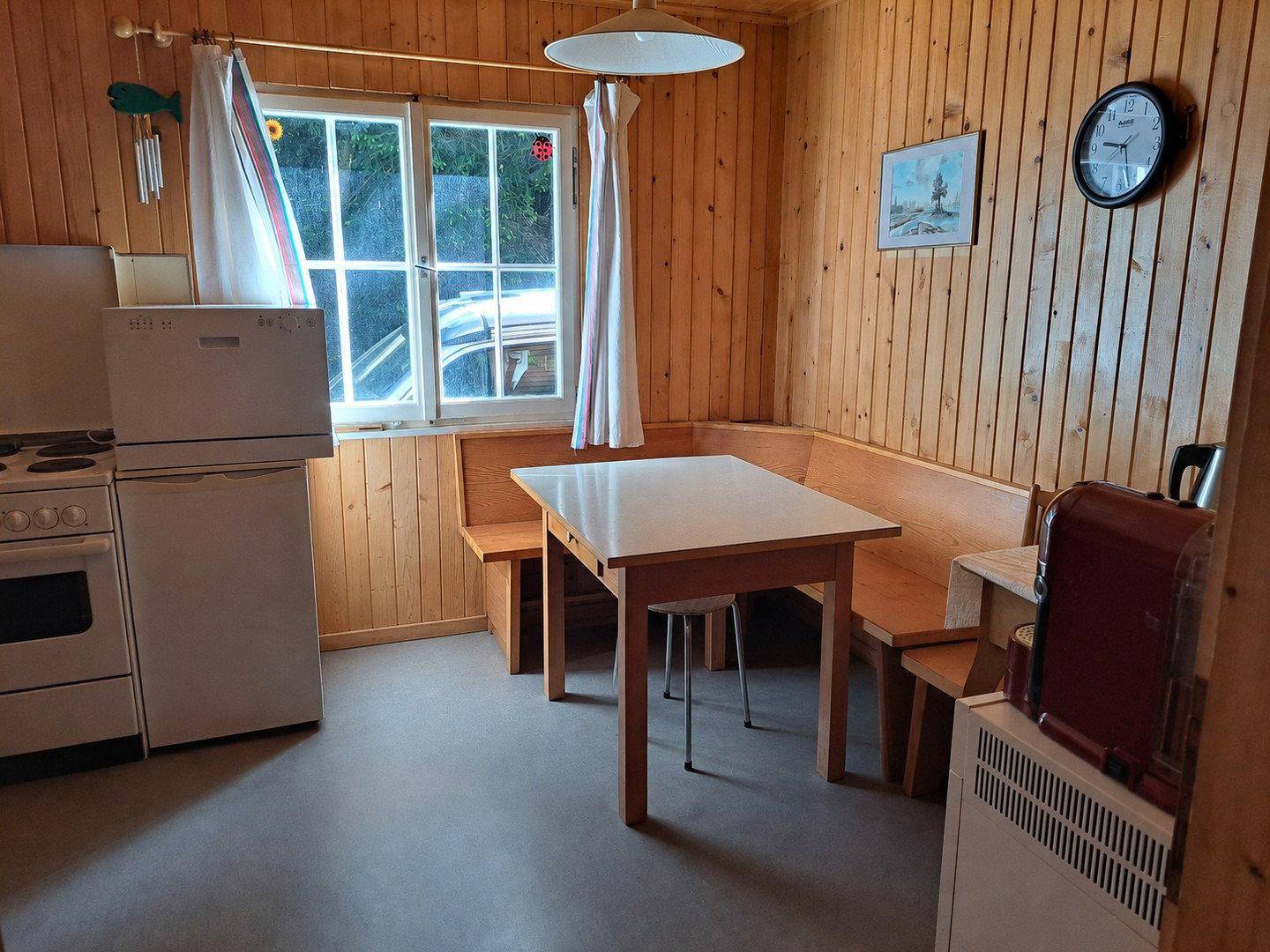 Rustikale Küche mit Holztisch, Eckbank und einfacher Ausstattung, umgeben von Holzvertäfelung.
