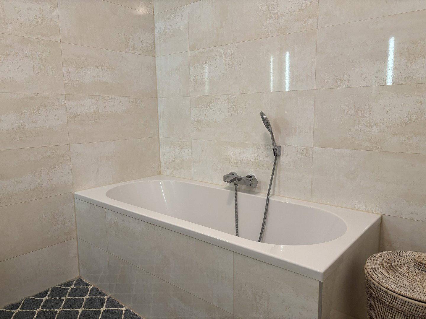 Helles Badezimmer mit beiger Fliesenwand und integrierter Badewanne.