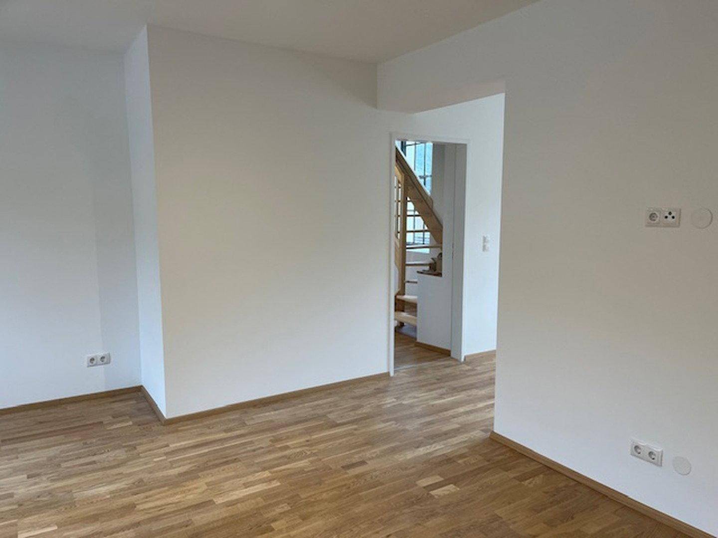 Heller, leerer Wohnraum mit Holzboden und Blick auf den Treppenaufgang.