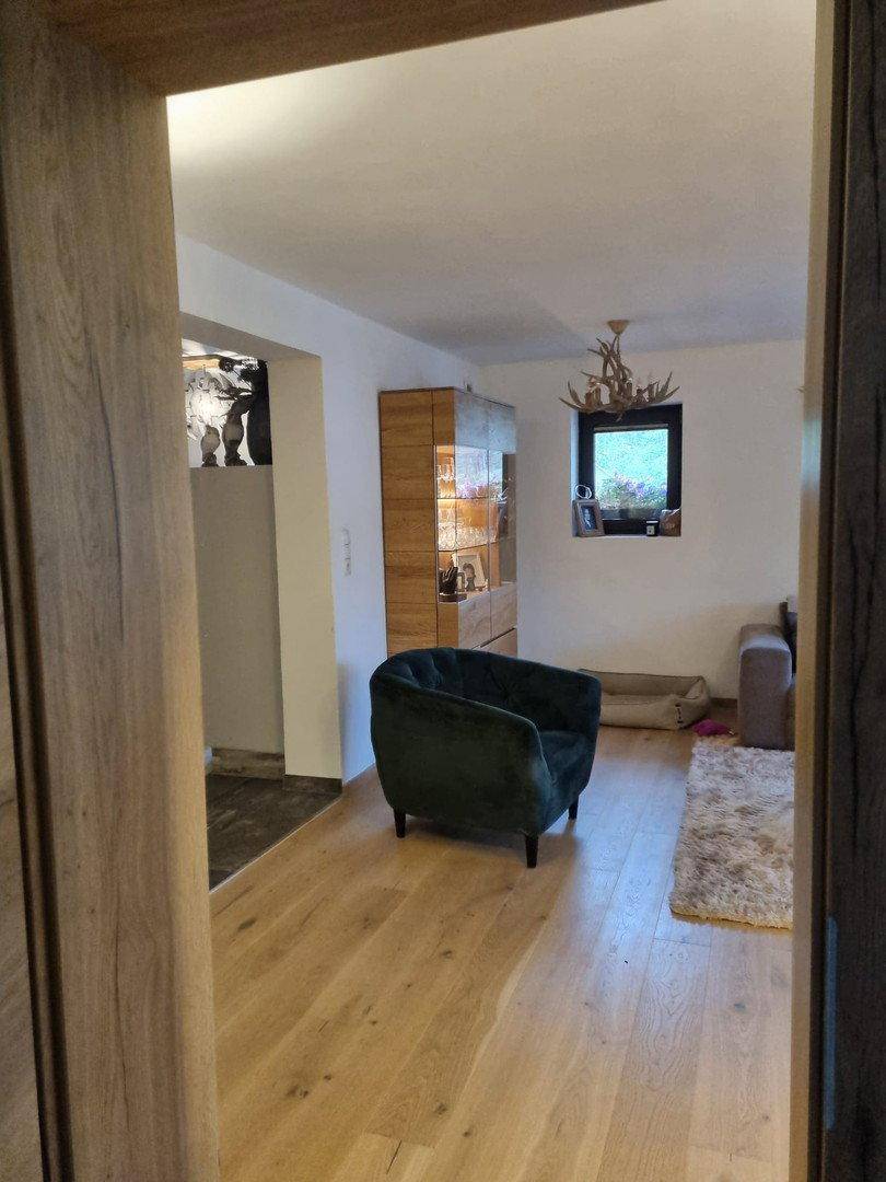 Heller Wohnbereich mit Holzboden, grünem Sessel und Blick in den angrenzenden Essbereich.