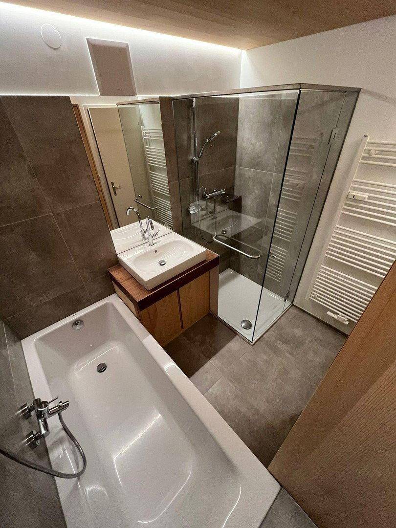 Modernes Badezimmer mit Badewanne, Duschkabine, Einzelwaschbecken und beheiztem Handtuchhalter.