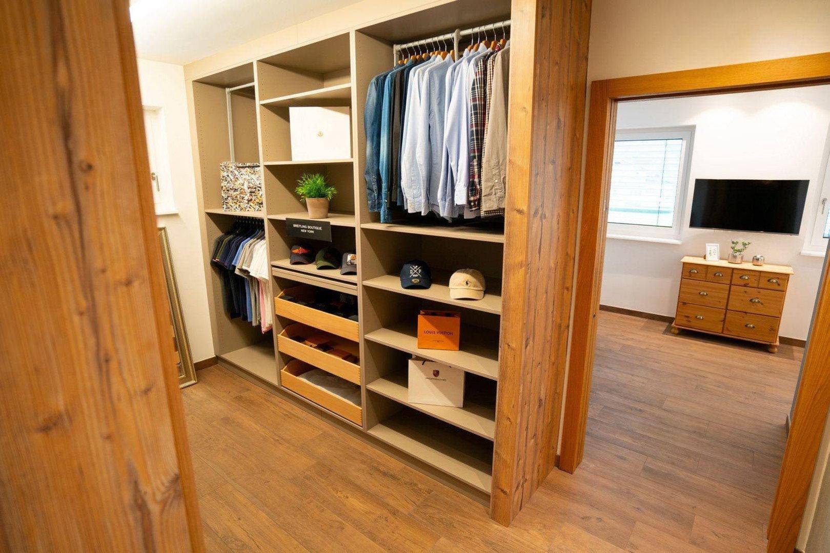 Heller begehbarer Kleiderschrank mit maßgefertigten Regalen und Blick ins Schlafzimmer.