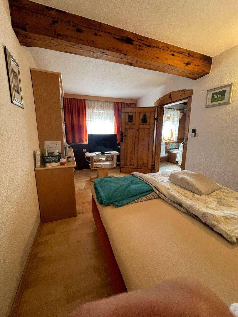 Gemütliches Schlafzimmer mit Holzbalken, Holzboden und Zugang zu einem weiteren Raum.