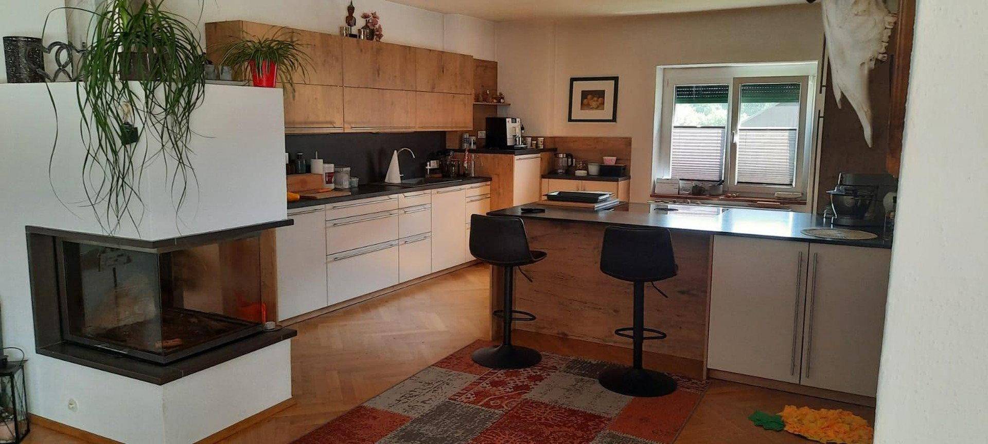 Moderne Küche mit Holzelementen, weißer Front, Kücheninsel und integriertem Kamin für gemütliche Abende.