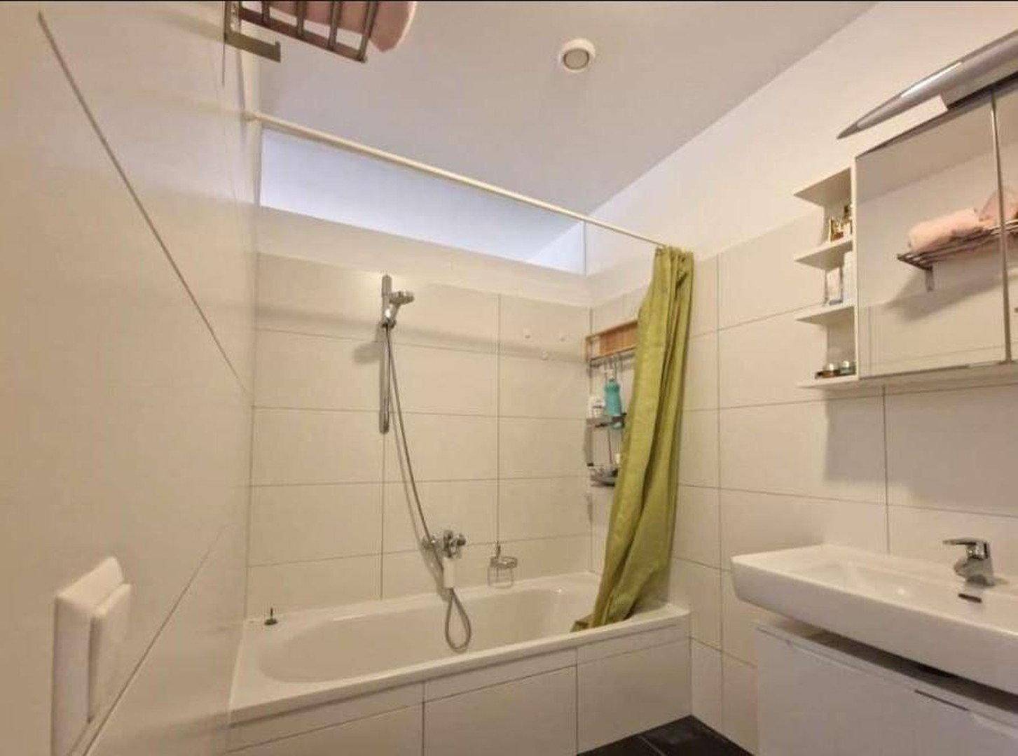 Funktionales Badezimmer mit Badewanne, Duschvorhang und weißen Fliesen.