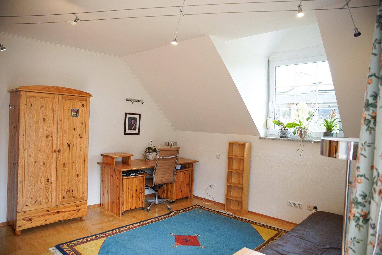 Helles Dachzimmer mit Schreibtisch, Holzmöbeln und schrägen Wänden, ideal als Büro oder Gästezimmer.