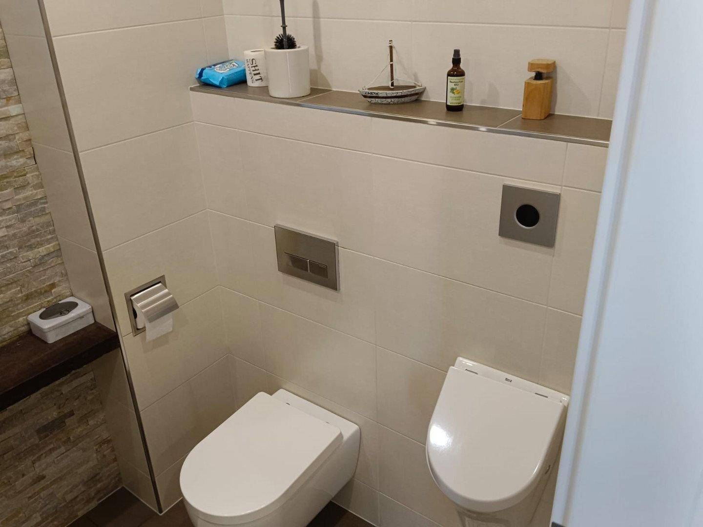 Modernes WC mit zwei wandhängenden Toiletten und beigefarbenen Fliesen.