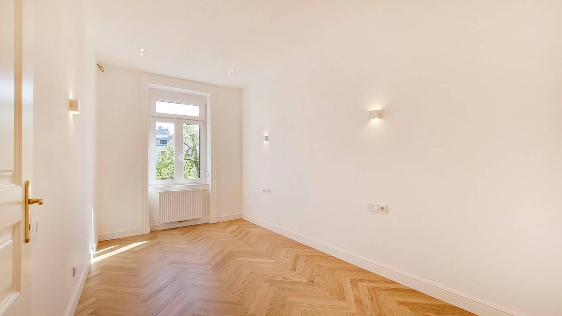 Helles Zimmer mit Fischgrätparkettboden und großem Fenster, ideal als Wohn- oder Schlafzimmer.