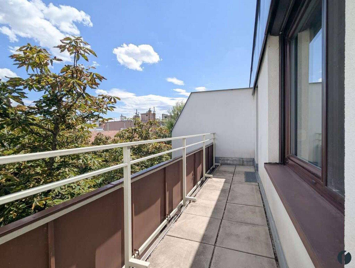 Schmaler Balkon mit Geländer und Blick ins Grüne, umgeben von Bäumen.
