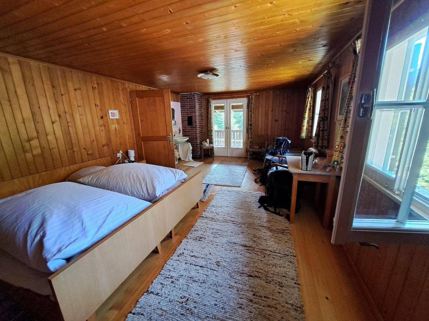 Helles Schlafzimmer mit Holzboden, Holzvertäfelung und Zugang zu einem Balkon.