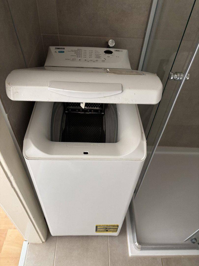 Nahaufnahme einer Toplader-Waschmaschine, die praktisch neben der Duschkabine platziert ist.