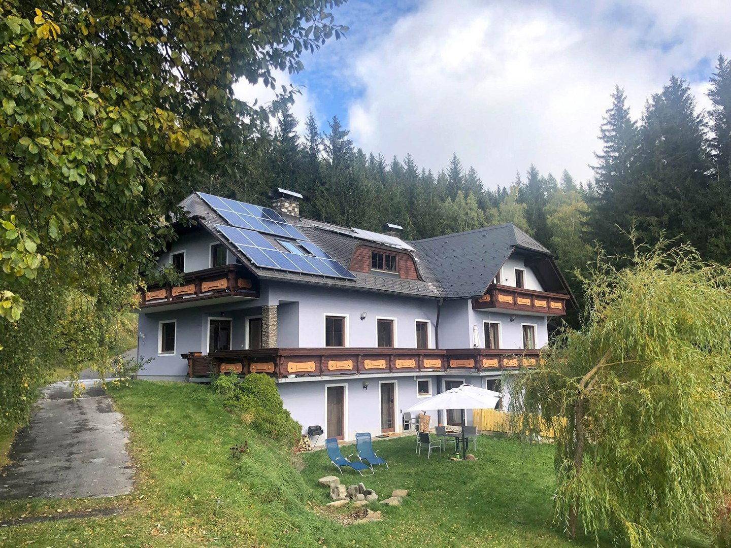 Haus mit Solaranlage, Balkonen und Gartenmöbeln, umgeben von Bäumen und Natur im Herbst.