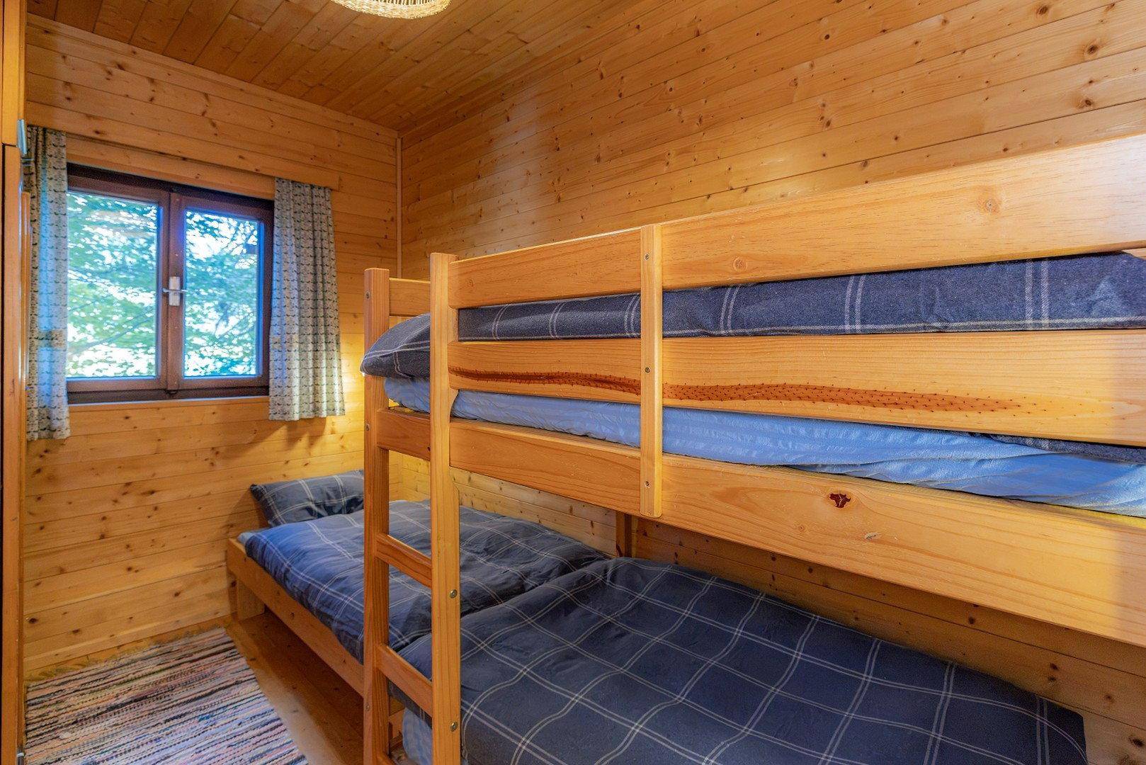 Gemütliches Schlafzimmer mit Holzvertäfelung, Etagenbetten und einem Fenster mit Waldblick.