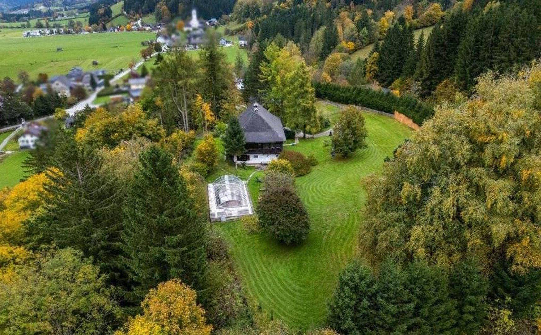 Weitläufiges Anwesen mit Haus, überdachtem Pool und umgebenden Wäldern und Bergen.