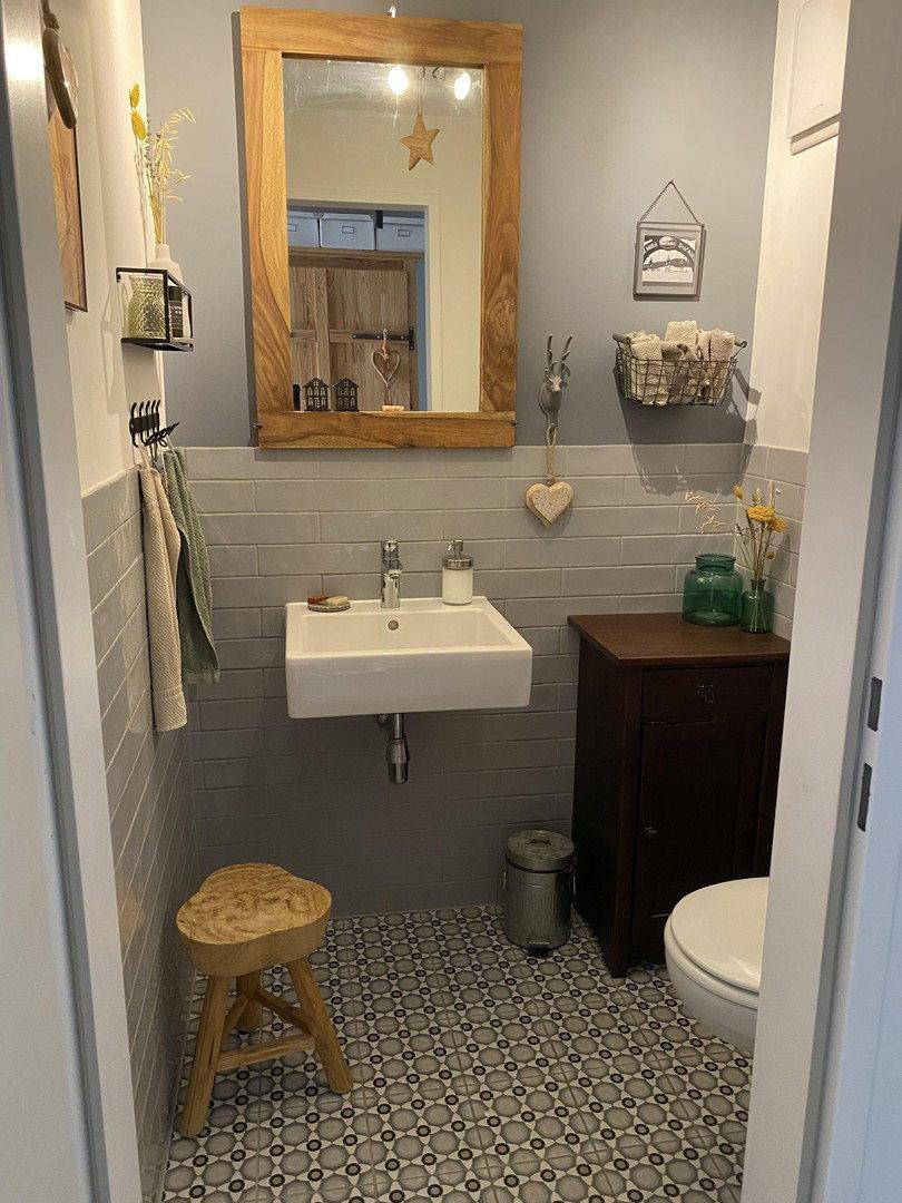 Modernes Gäste-WC mit kleinem Waschbecken, Holzspiegel und gemusterten Fliesen.