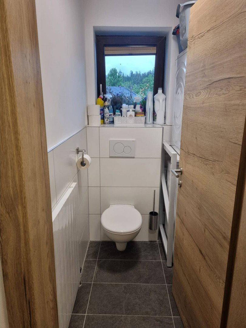 Kleines Gäste-WC mit Toilette, Fenster und Waschmaschine in hellem Design.